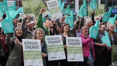 Eine Menschenmenge hält Plakate mit der Aufschrift „Bürger-Energie, Klimaschützer in Aktion“ hoch.