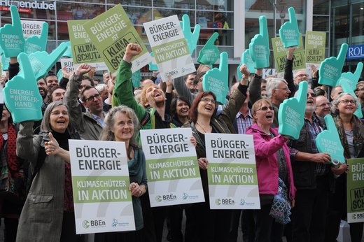 Eine Menschenmenge hält Plakate mit der Aufschrift „Bürger-Energie, Klimaschützer in Aktion“ hoch.